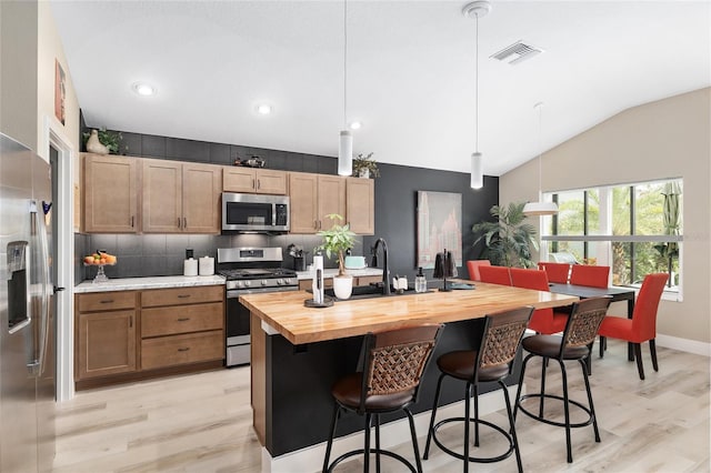 kitchen with visible vents, a kitchen breakfast bar, stainless steel appliances, wooden counters, and vaulted ceiling