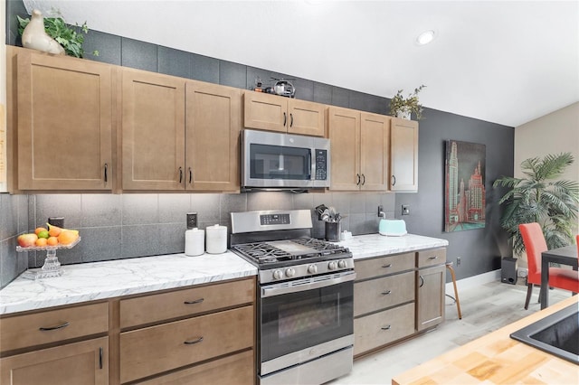 kitchen featuring backsplash, stainless steel appliances, light wood-type flooring, and baseboards