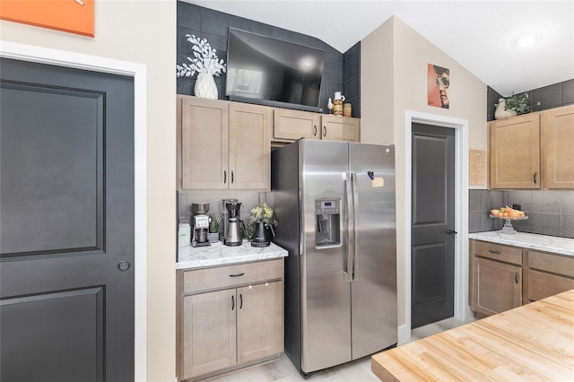 kitchen featuring tasteful backsplash, light stone counters, and stainless steel refrigerator with ice dispenser