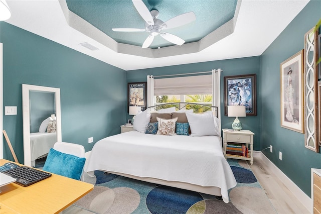 bedroom featuring a ceiling fan, wood finished floors, visible vents, baseboards, and a raised ceiling