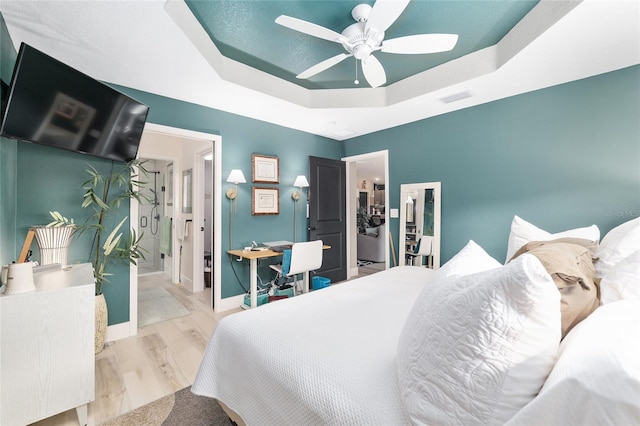 bedroom featuring a ceiling fan, wood finished floors, visible vents, baseboards, and a raised ceiling