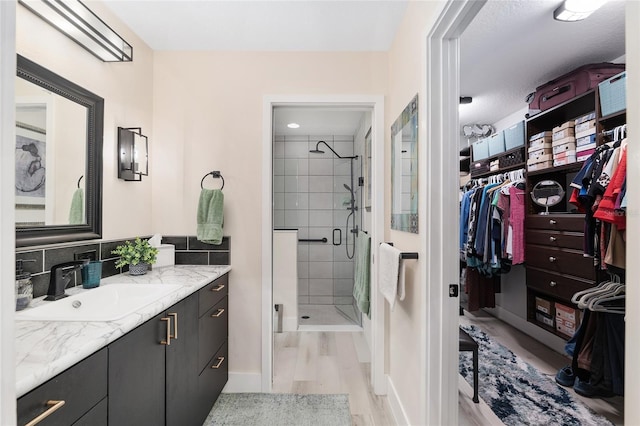 bathroom featuring a stall shower, tasteful backsplash, wood finished floors, a spacious closet, and vanity