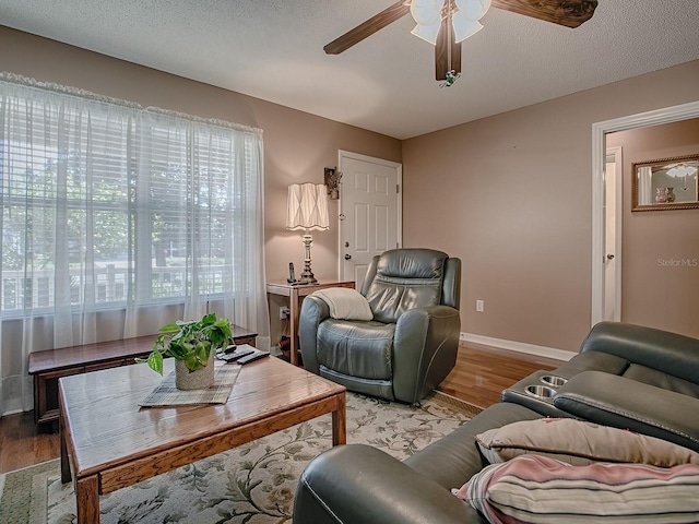 living area featuring a textured ceiling, baseboards, a ceiling fan, and wood finished floors