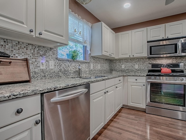 kitchen featuring a sink, tasteful backsplash, appliances with stainless steel finishes, white cabinets, and light wood finished floors