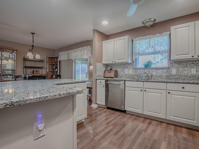 kitchen featuring light wood-type flooring, light stone counters, backsplash, stainless steel dishwasher, and white cabinets