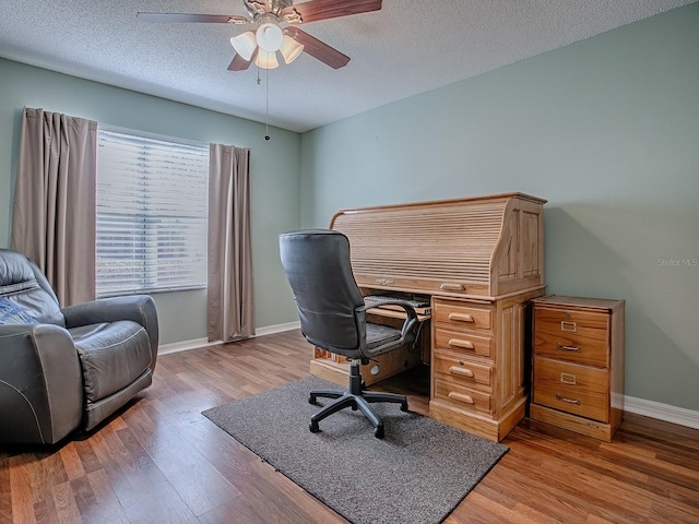 office area featuring a textured ceiling, baseboards, light wood finished floors, and ceiling fan