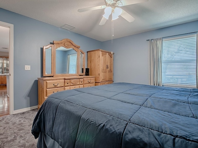 carpeted bedroom with a textured ceiling, baseboards, and a ceiling fan