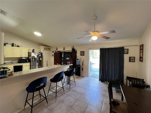 kitchen featuring a breakfast bar area, ceiling fan, vaulted ceiling, black microwave, and stainless steel fridge