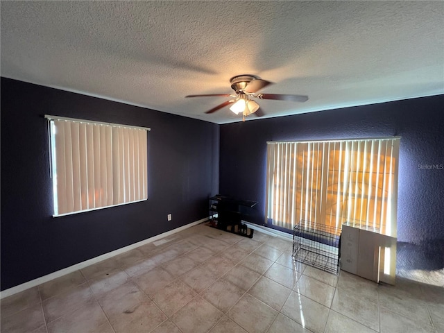 unfurnished room featuring a ceiling fan, baseboards, a textured wall, and a textured ceiling