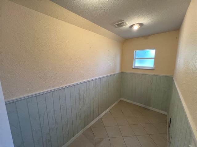 spare room featuring visible vents, a textured ceiling, wooden walls, wainscoting, and a textured wall