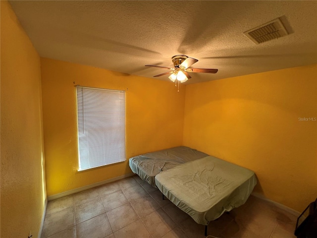 bedroom with visible vents, a textured ceiling, light tile patterned flooring, baseboards, and ceiling fan