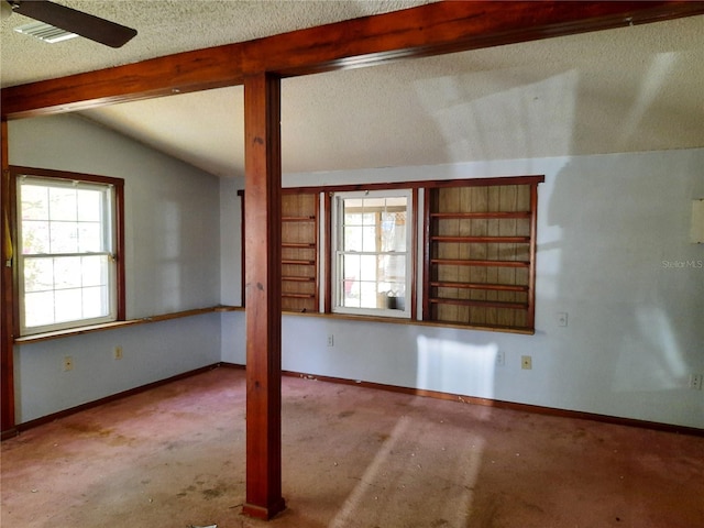 empty room with lofted ceiling with beams, baseboards, plenty of natural light, and a textured ceiling