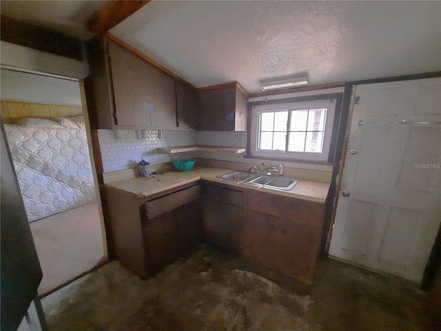 kitchen with light countertops, concrete floors, backsplash, and a sink