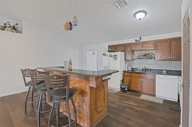 kitchen featuring a sink, dark countertops, dark wood finished floors, white appliances, and a breakfast bar area