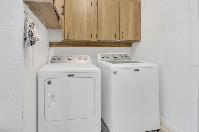 laundry area featuring washer and clothes dryer, cabinet space, and a textured wall