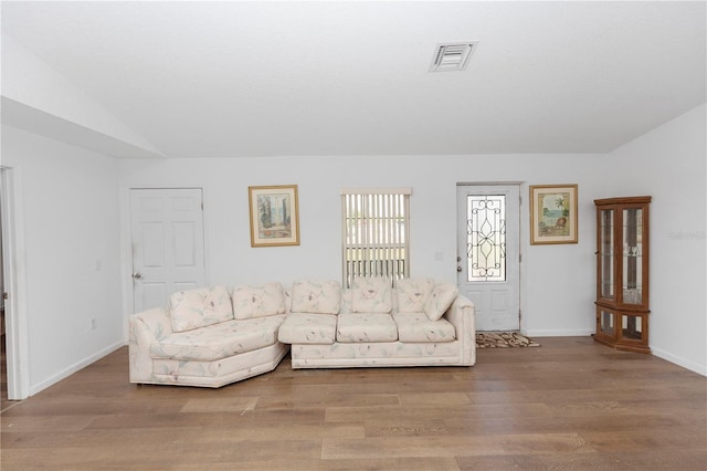living area with vaulted ceiling, visible vents, wood finished floors, and baseboards