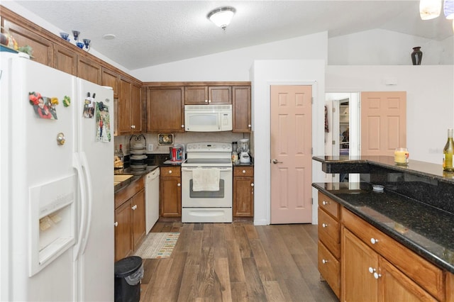 kitchen with brown cabinets, dark stone counters, dark wood finished floors, white appliances, and lofted ceiling