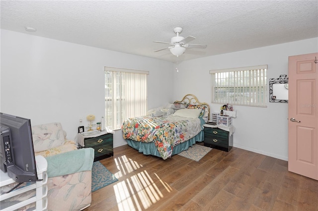bedroom with ceiling fan, a textured ceiling, multiple windows, and wood finished floors