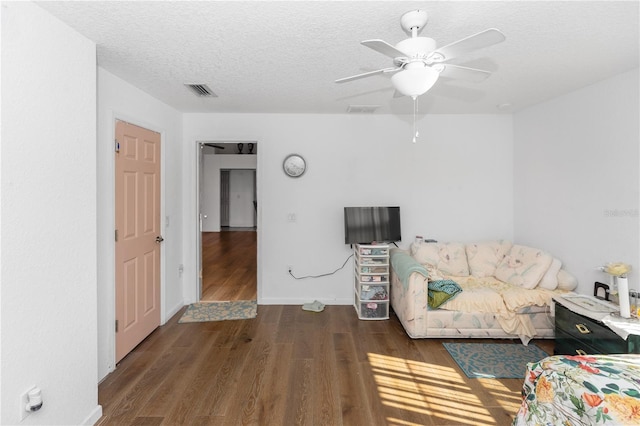 living room featuring a textured ceiling, baseboards, ceiling fan, visible vents, and wood finished floors