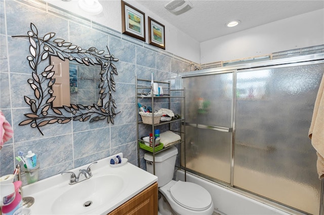 full bathroom featuring tile walls, a textured ceiling, bath / shower combo with glass door, toilet, and vanity