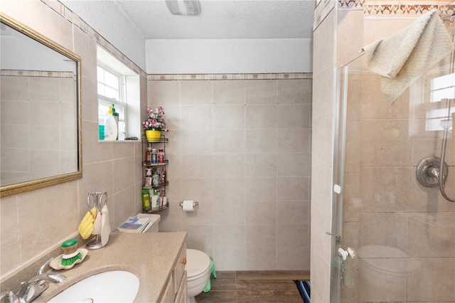 full bathroom featuring a stall shower, vanity, tile walls, and toilet