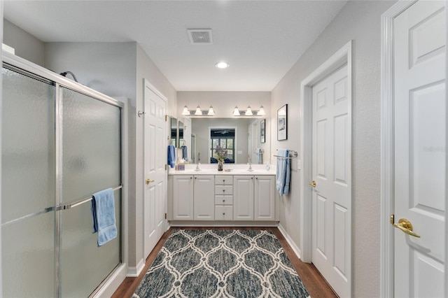 bathroom with double vanity, visible vents, wood finished floors, and a shower stall