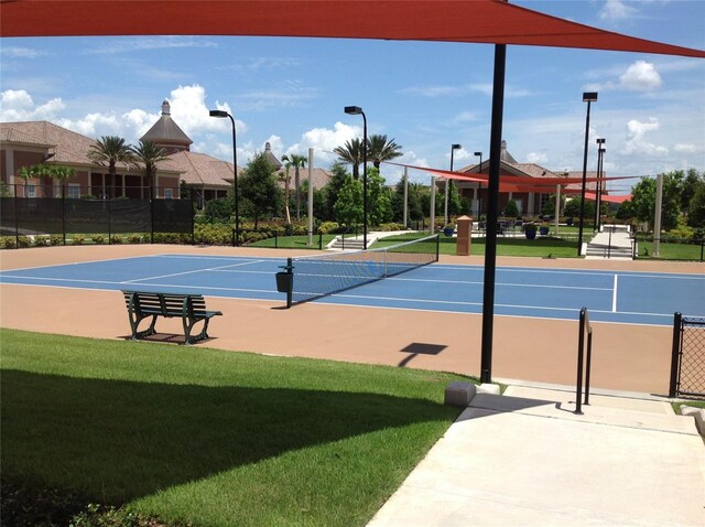 view of tennis court featuring community basketball court, fence, and a lawn