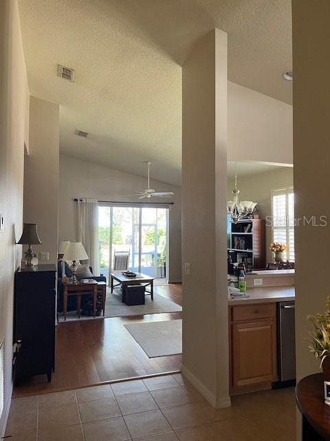 interior space featuring light tile patterned flooring, a textured ceiling, vaulted ceiling, and visible vents