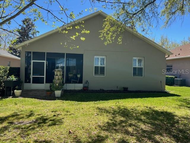 rear view of house featuring central AC, a sunroom, a yard, and stucco siding