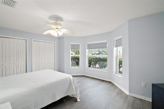 bedroom featuring visible vents, two closets, baseboards, ceiling fan, and wood finished floors