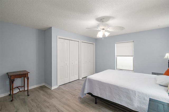 bedroom with two closets, baseboards, a textured ceiling, a ceiling fan, and wood finished floors