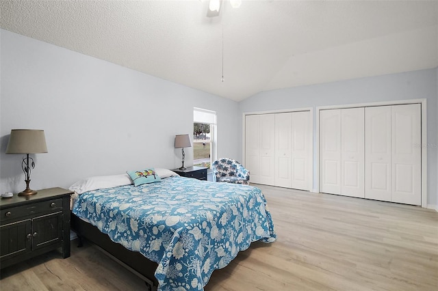 bedroom with lofted ceiling, light wood-style flooring, multiple closets, a textured ceiling, and a ceiling fan