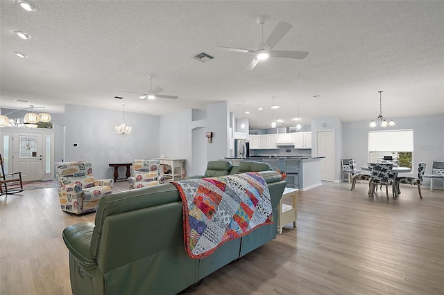 living room featuring ceiling fan with notable chandelier, visible vents, light wood-style floors, and a textured ceiling