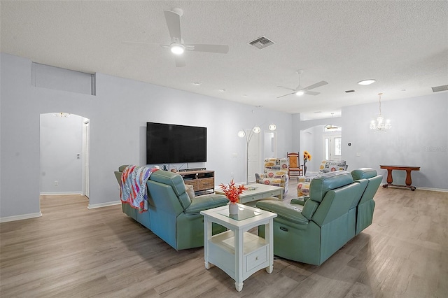 living area with light wood-style flooring, arched walkways, ceiling fan with notable chandelier, and visible vents
