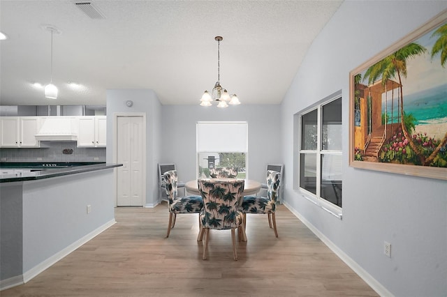 dining area with a chandelier, lofted ceiling, baseboards, visible vents, and light wood-style floors
