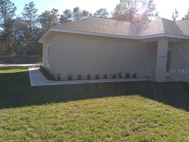 view of side of home with stucco siding, a lawn, and a shingled roof