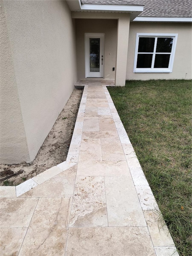 entrance to property with stucco siding, a yard, and a shingled roof