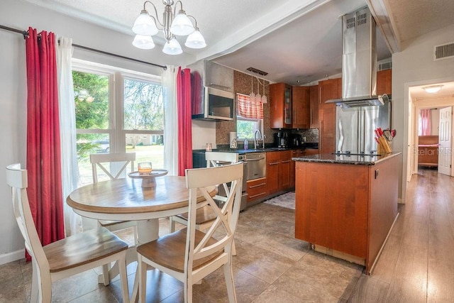 kitchen featuring a chandelier, dark countertops, brown cabinets, decorative backsplash, and island range hood