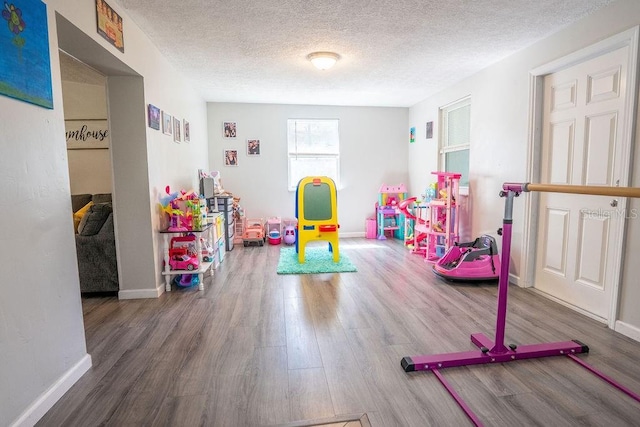 game room with a textured ceiling, baseboards, and wood finished floors