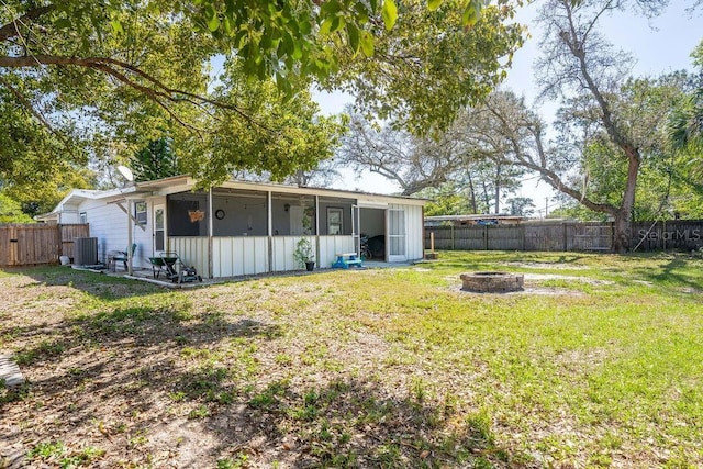 rear view of house with central AC unit, an outdoor fire pit, a fenced backyard, and a lawn