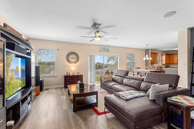 living area featuring light wood-type flooring, a healthy amount of sunlight, a ceiling fan, and visible vents