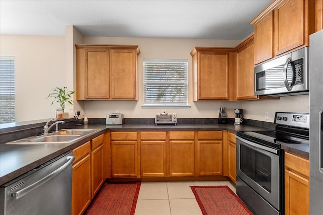 kitchen with appliances with stainless steel finishes, light tile patterned flooring, a sink, and dark countertops