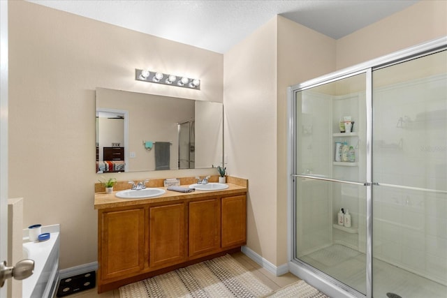 ensuite bathroom featuring a sink, tile patterned floors, a shower stall, and double vanity