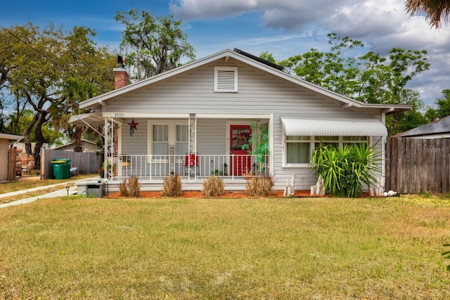 bungalow-style home featuring a front lawn, fence, covered porch, and a chimney