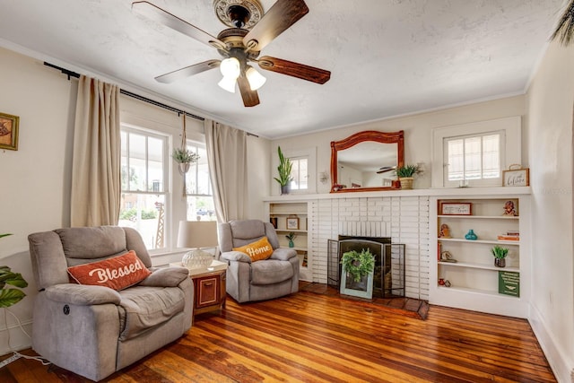 sitting room with a brick fireplace, ceiling fan, ornamental molding, and hardwood / wood-style flooring