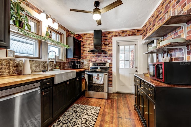 kitchen featuring a sink, appliances with stainless steel finishes, butcher block countertops, and wall chimney exhaust hood