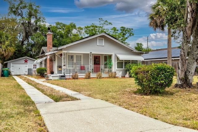 bungalow-style house featuring a porch, a chimney, a front yard, a detached garage, and an outdoor structure