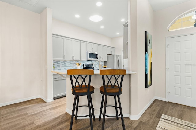 6152 Topsail Rd, Lady Lake, FL 32159 - kitchen with light countertops, a breakfast bar, backsplash, light wood-style flooring, and appliances with stainless steel finishes