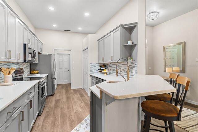 6152 Topsail Rd, Lady Lake, FL 32159 - kitchen featuring a peninsula, appliances with stainless steel finishes, open shelves, gray cabinetry, and a breakfast bar area