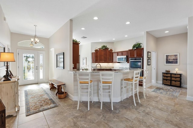 kitchen with backsplash, decorative light fixtures, a breakfast bar area, a peninsula, and stainless steel appliances